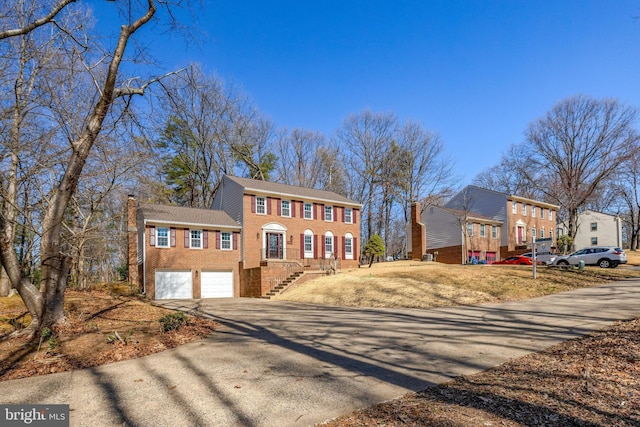 colonial house featuring brick siding, driveway, a chimney, and a garage