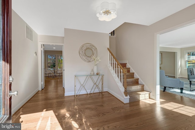 foyer featuring visible vents, baseboards, stairs, wood finished floors, and a notable chandelier