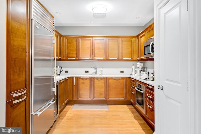 kitchen with a sink, stainless steel appliances, brown cabinets, and light wood-style floors