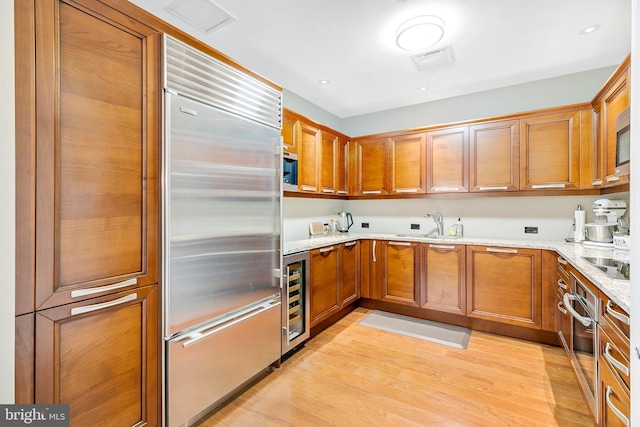 kitchen featuring light stone counters, light wood-style flooring, appliances with stainless steel finishes, brown cabinetry, and beverage cooler