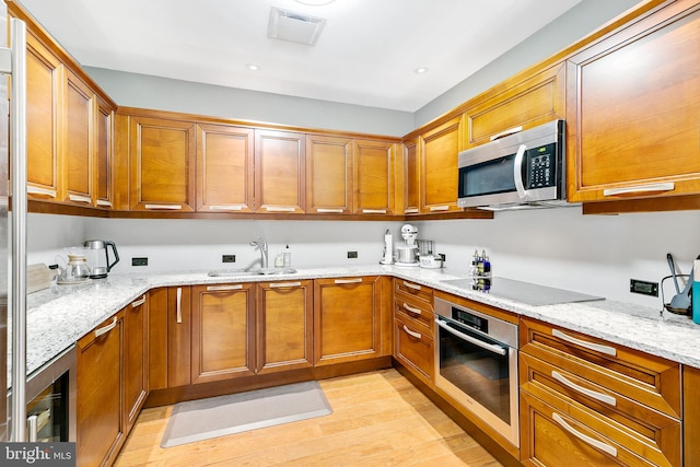 kitchen with appliances with stainless steel finishes, brown cabinetry, a sink, and light stone counters