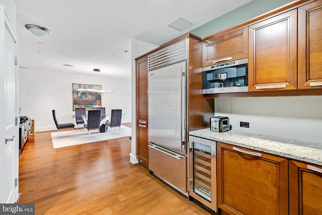 kitchen with visible vents, wine cooler, light stone counters, built in refrigerator, and light wood-type flooring