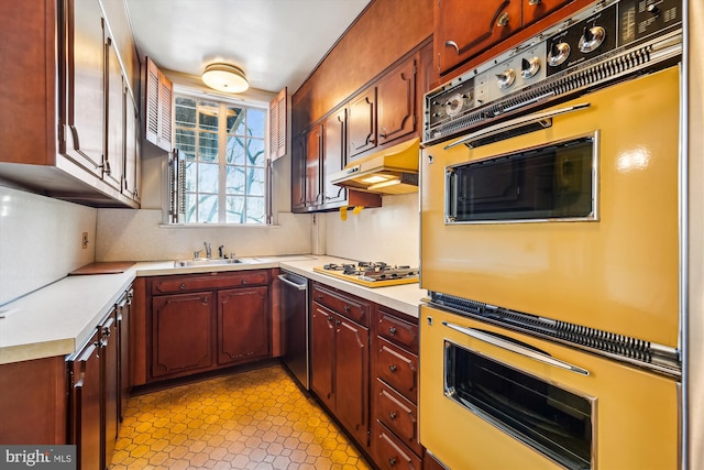 kitchen with white gas stovetop, light countertops, under cabinet range hood, double oven, and a sink