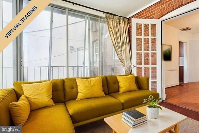 living area with brick wall, wood finished floors, and visible vents