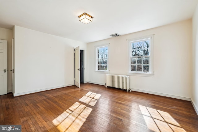 spare room with baseboards, hardwood / wood-style floors, visible vents, and radiator