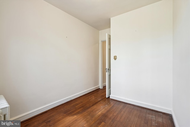 spare room featuring radiator heating unit, dark wood-style flooring, and baseboards