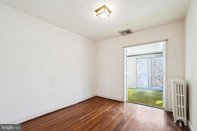 empty room with radiator heating unit, visible vents, dark wood finished floors, and baseboards