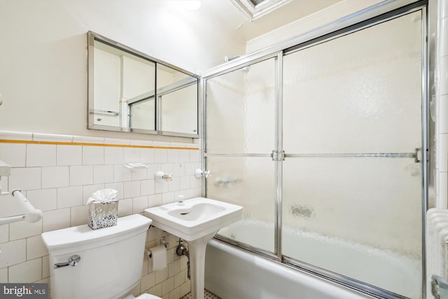 bathroom featuring toilet, combined bath / shower with glass door, and tile walls