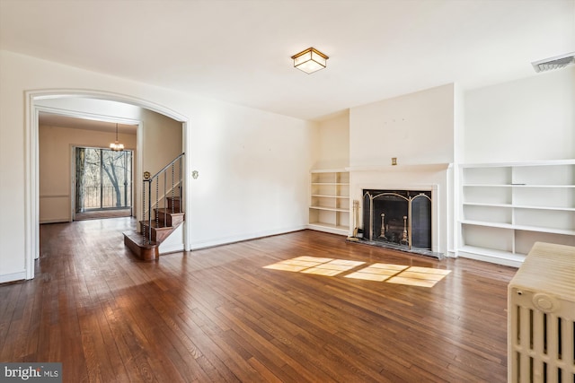 unfurnished living room featuring visible vents, a fireplace with raised hearth, baseboards, wood-type flooring, and stairway