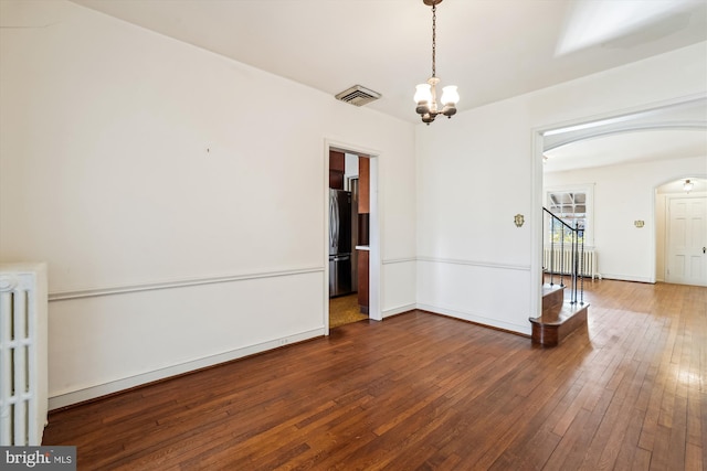 empty room featuring arched walkways, hardwood / wood-style flooring, visible vents, and radiator