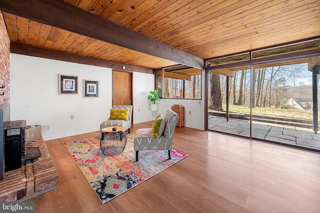 living area with beam ceiling, wood ceiling, a wood stove, and wood finished floors