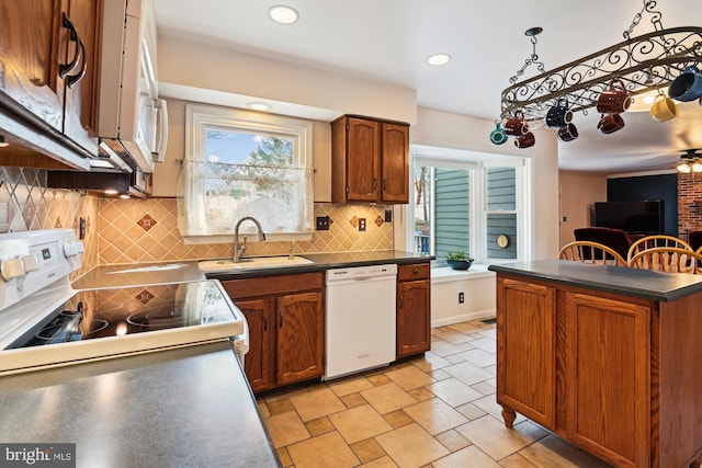 kitchen featuring white appliances, brown cabinetry, dark countertops, and a sink