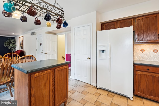 kitchen featuring backsplash, dark countertops, white fridge with ice dispenser, brown cabinetry, and crown molding