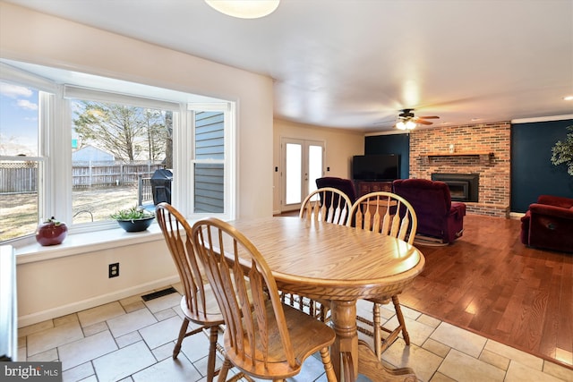 dining space featuring visible vents, a brick fireplace, baseboards, ceiling fan, and light wood-style flooring