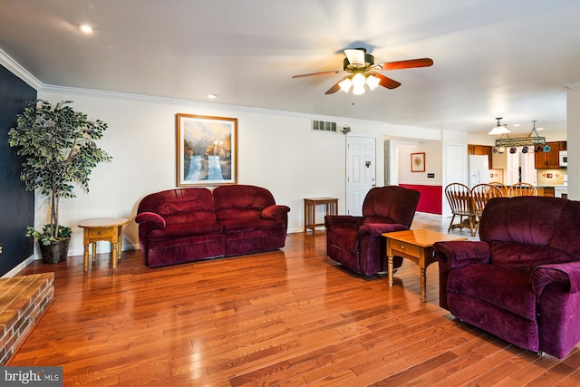 living room with a ceiling fan, baseboards, wood finished floors, visible vents, and ornamental molding