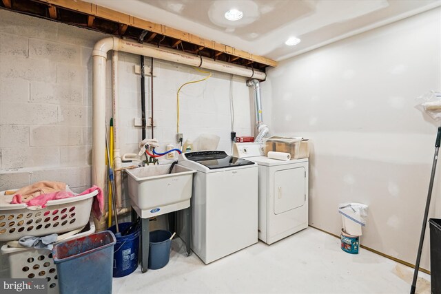 clothes washing area featuring laundry area, washing machine and dryer, concrete block wall, and a sink