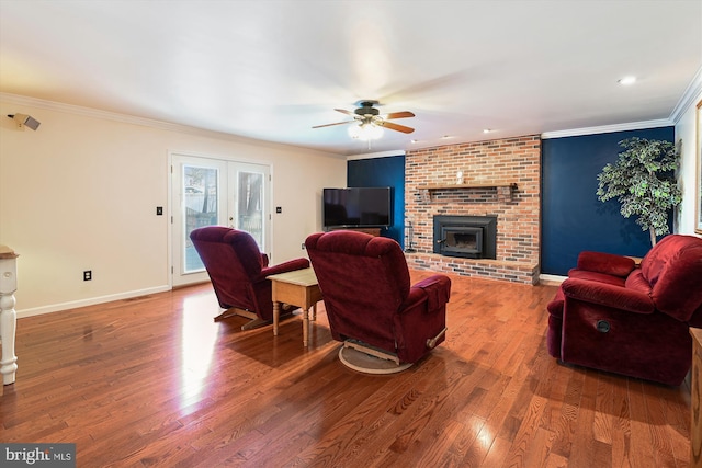 living room featuring wood finished floors, baseboards, ceiling fan, crown molding, and a brick fireplace