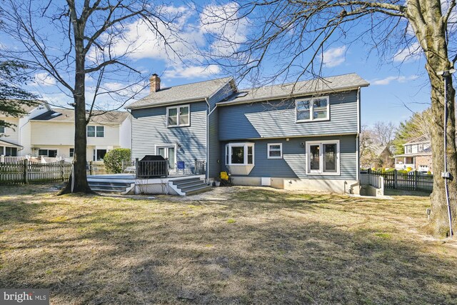 rear view of house featuring a wooden deck, fence, a lawn, and a chimney