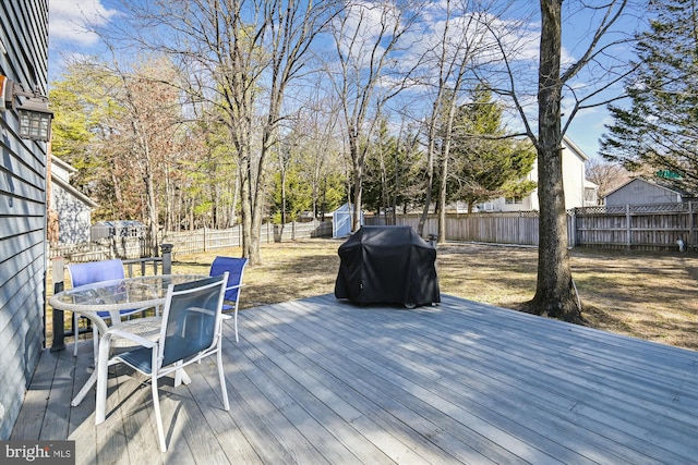 wooden deck featuring grilling area, outdoor dining area, an outdoor structure, a fenced backyard, and a storage unit