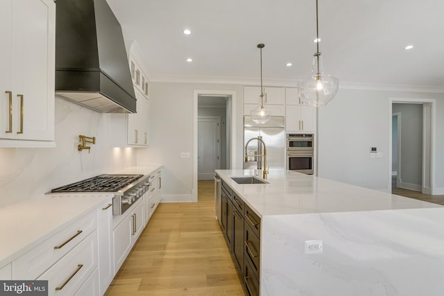 kitchen featuring pendant lighting, custom exhaust hood, appliances with stainless steel finishes, white cabinetry, and a sink