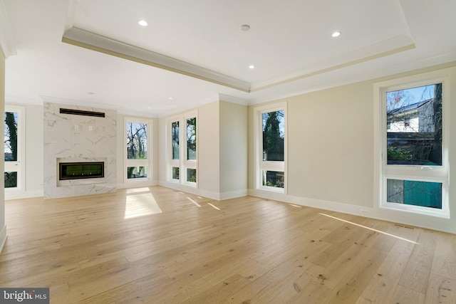 unfurnished living room featuring ornamental molding, light wood finished floors, a premium fireplace, and a raised ceiling