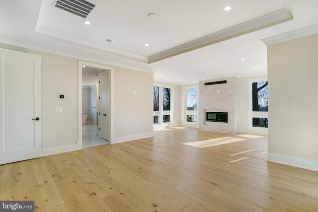 unfurnished living room featuring light wood-style floors, a raised ceiling, and a premium fireplace