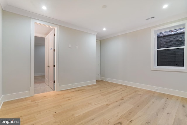 empty room with baseboards, light wood finished floors, visible vents, and crown molding