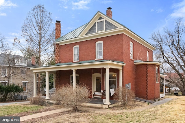 view of front of home featuring brick siding, a chimney, a porch, a standing seam roof, and metal roof