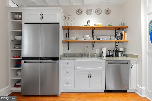 kitchen with open shelves, appliances with stainless steel finishes, white cabinets, a sink, and light stone countertops