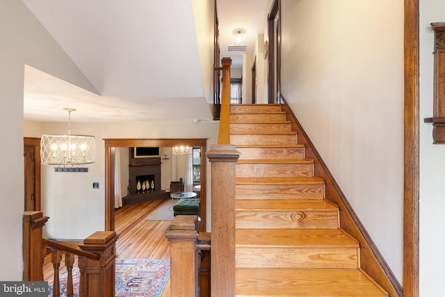 staircase with a fireplace, visible vents, an inviting chandelier, vaulted ceiling, and wood finished floors