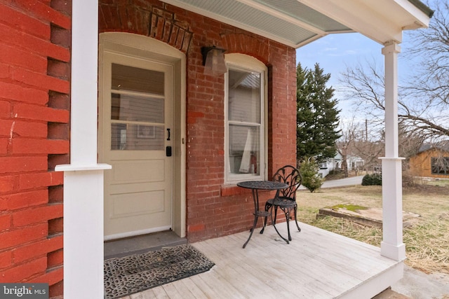 view of exterior entry featuring a porch and brick siding