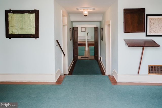 hall with carpet flooring, an upstairs landing, visible vents, and baseboards