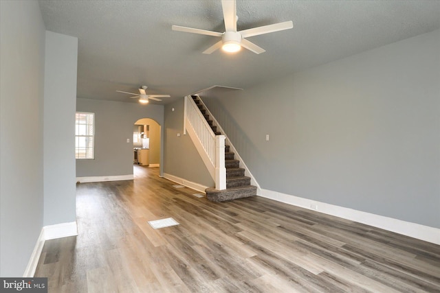 unfurnished living room with arched walkways, a ceiling fan, wood finished floors, baseboards, and stairs