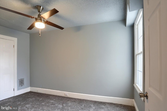 unfurnished room featuring dark carpet, plenty of natural light, a textured ceiling, and baseboards