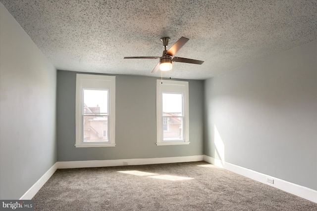 carpeted spare room featuring a textured ceiling, ceiling fan, and baseboards
