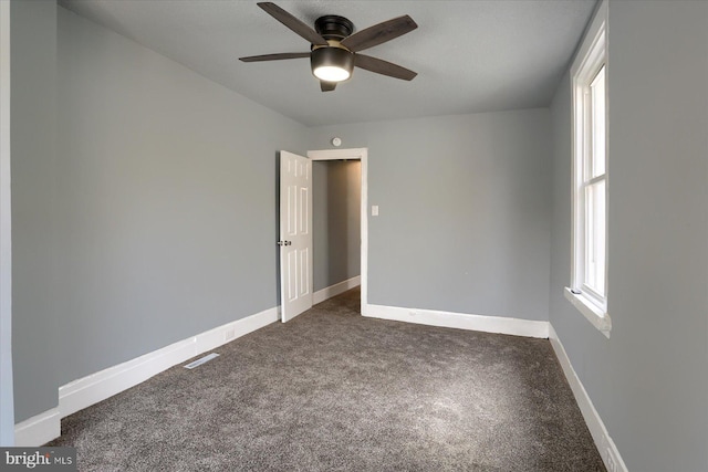 empty room with ceiling fan, dark carpet, visible vents, and baseboards