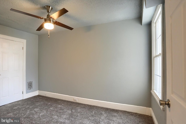 empty room with baseboards, dark carpet, ceiling fan, and a textured ceiling