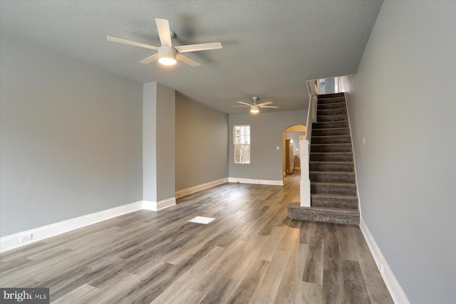 unfurnished living room with arched walkways, wood finished floors, baseboards, and stairs