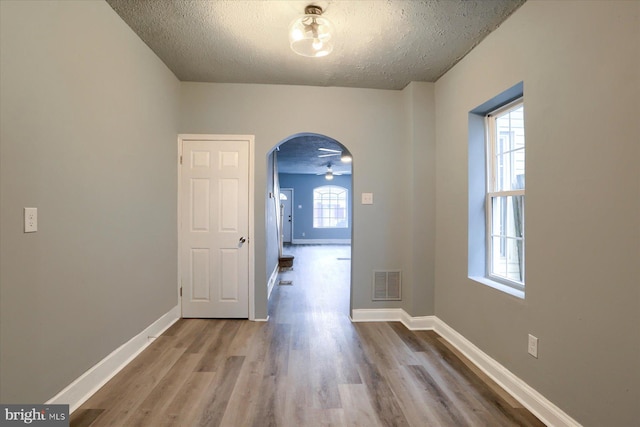 unfurnished dining area featuring baseboards, visible vents, arched walkways, wood finished floors, and a textured ceiling
