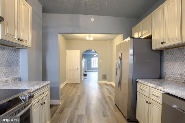 kitchen featuring arched walkways, stainless steel appliances, visible vents, baseboards, and light wood finished floors