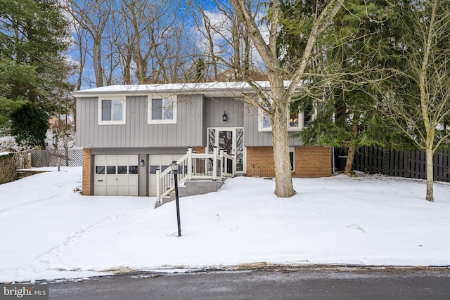 raised ranch with a garage, brick siding, and fence