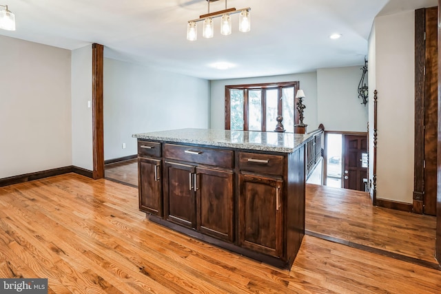 kitchen with baseboards, light wood-style flooring, a kitchen island, decorative light fixtures, and light stone countertops