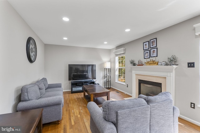 living area with baseboards, a glass covered fireplace, light wood-style flooring, and recessed lighting