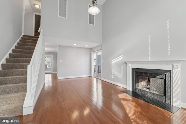 unfurnished living room featuring a fireplace with flush hearth, a towering ceiling, baseboards, stairway, and wood-type flooring