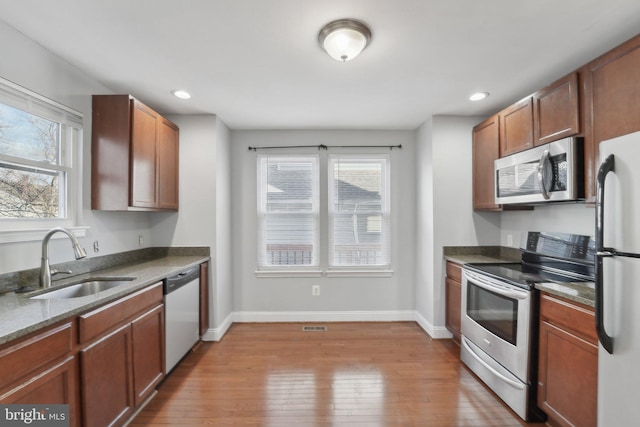 kitchen featuring a sink, baseboards, appliances with stainless steel finishes, dark stone counters, and hardwood / wood-style floors