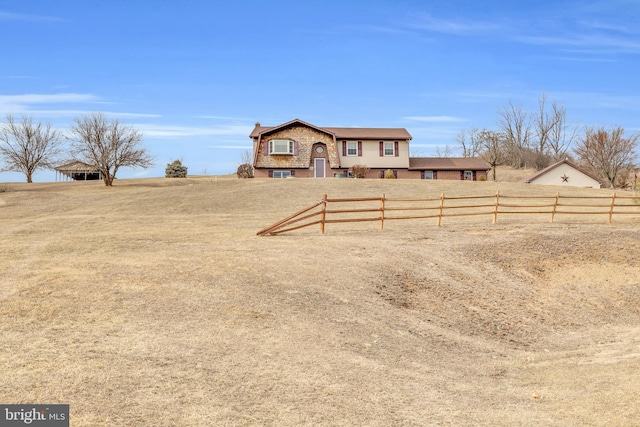 view of front of home with brick siding, a front yard, fence, and a rural view