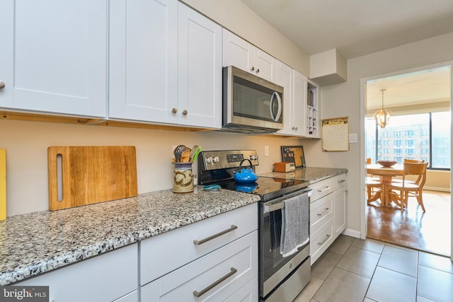 kitchen with light tile patterned floors, white cabinets, appliances with stainless steel finishes, light stone countertops, and a notable chandelier