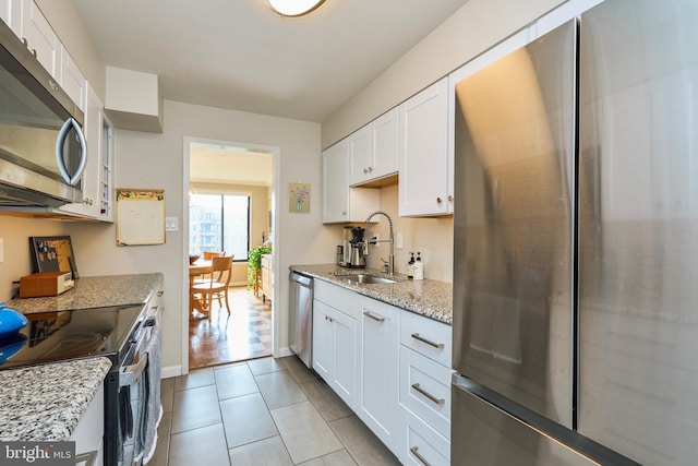 kitchen with light tile patterned floors, appliances with stainless steel finishes, light stone countertops, white cabinetry, and a sink