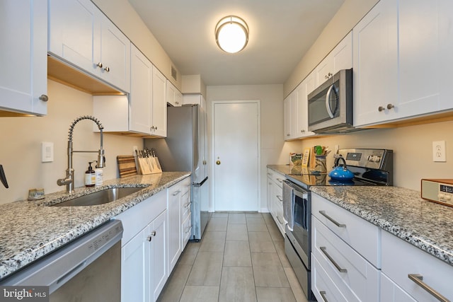 kitchen featuring stainless steel appliances, light stone counters, a sink, and white cabinets