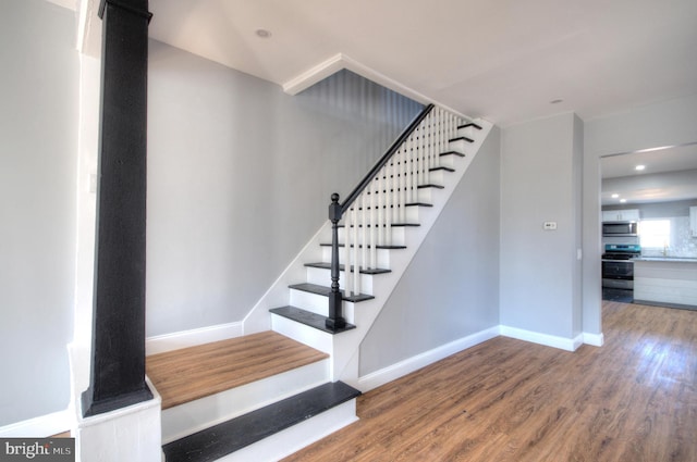 stairs with baseboards, wood finished floors, and recessed lighting